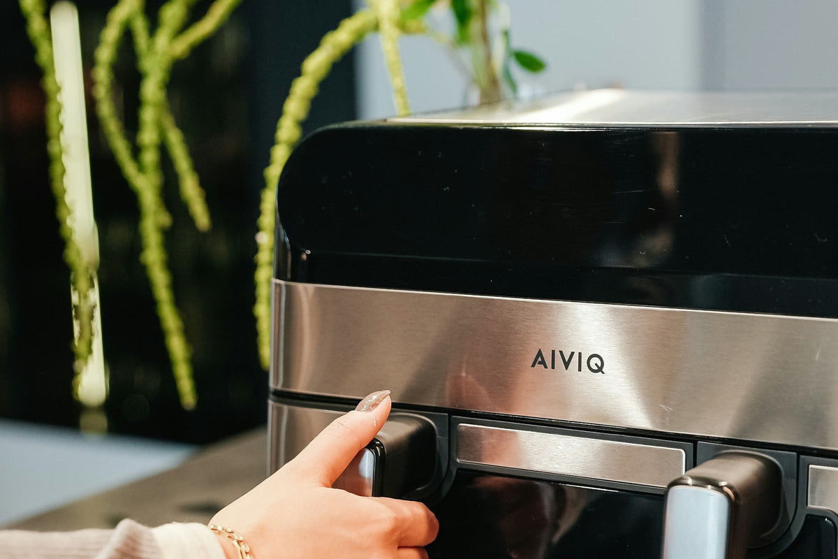 En hand tar tag i handtaget på en låda i en AIVIQ Premio Dual på en köksbänk, med gröna kvistar i bakgrunden