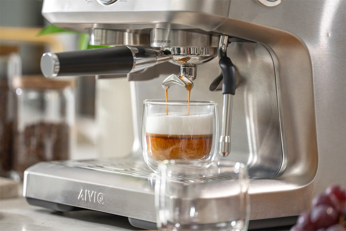 Espresso rinner från portafiltrets två utlopp ner i ett glas med varm mjölk på en espressomaskin i stål