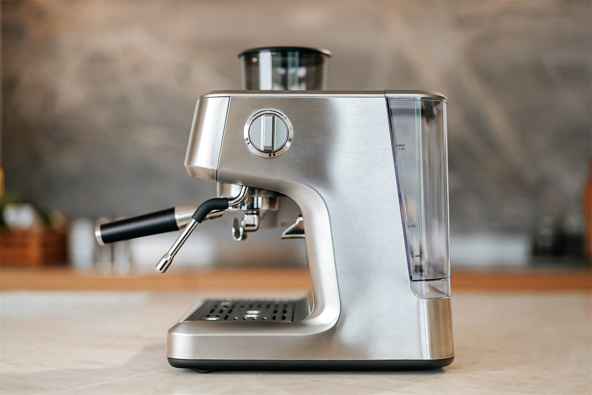 Espressomaskin i stål sedd från sidan med ångrör, portafilter och vattentank på en ljus köksbänk