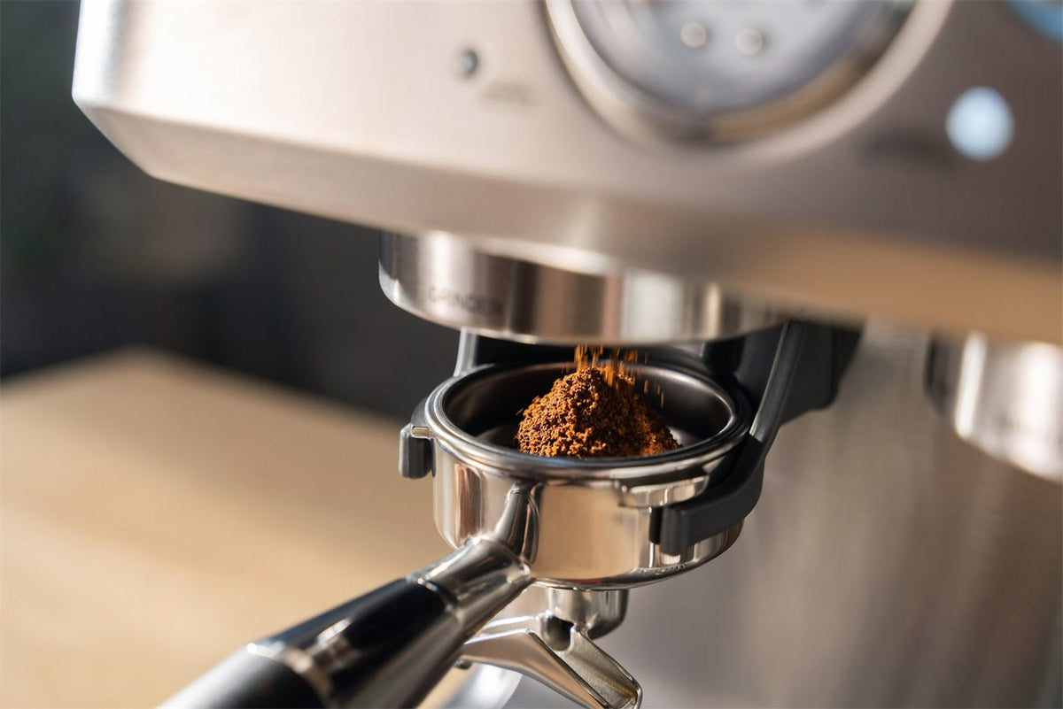 Malet kaffe faller ner i ett portafilter under kvarnen på en espressomaskin i stål