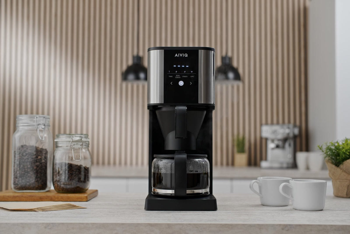 AIVIQ Grind 'N Brew Inspire med full glaskanna på en köksbänk, två glasburkar med kaffebönor och två vita koppar