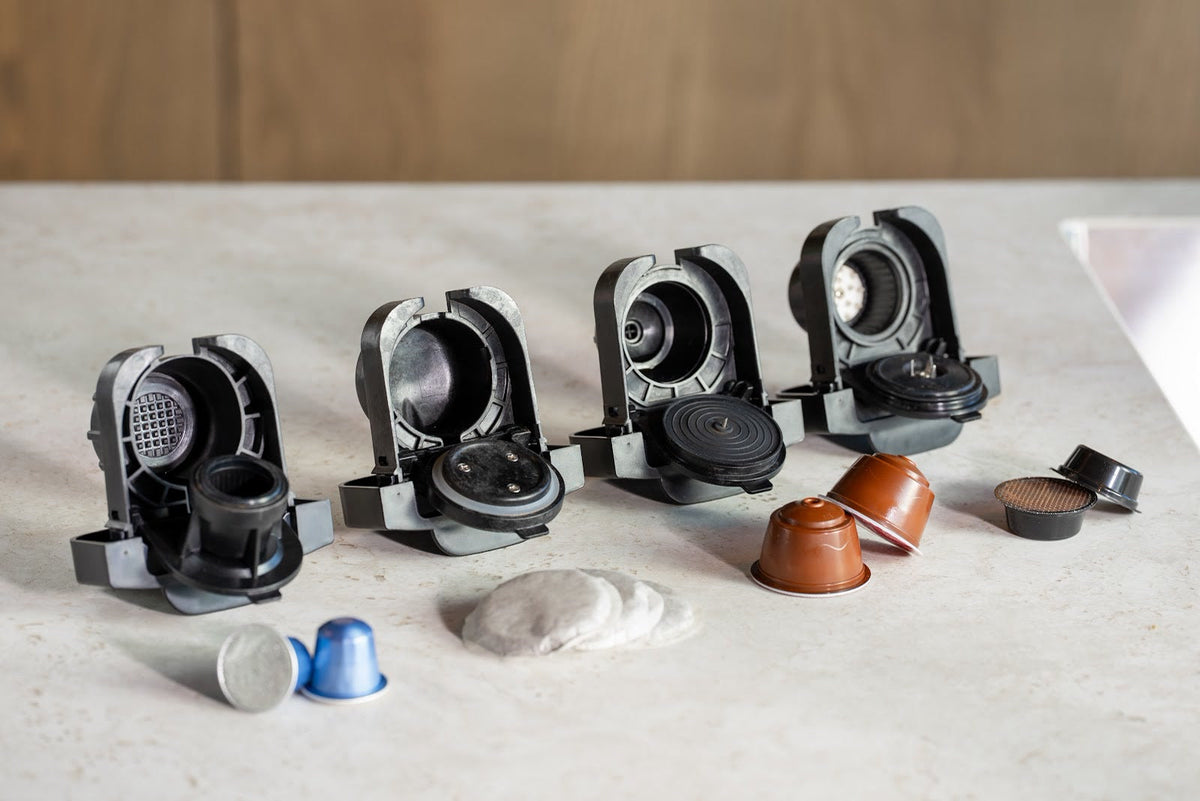 Fyra öppna kapseladaptrar på ett bord med kapslar i olika former och mjuka kaffepads
