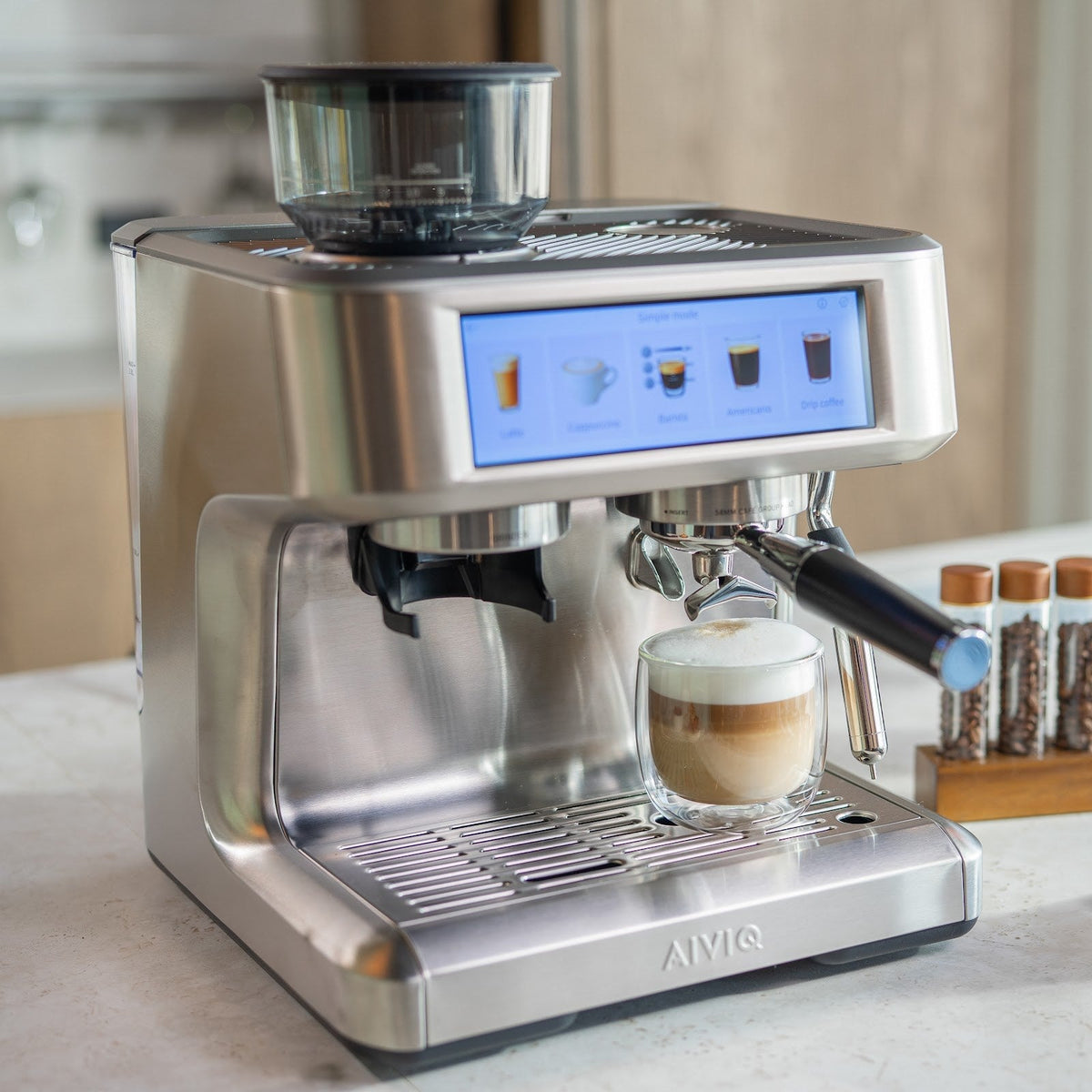Aspire Expert sedd snett från vänster med ett dubbelväggigt glas med kaffe och ett tjockt lager mjölkskum på droppbrickan. Skärmen står i Simple mode.